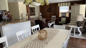 Uma área de refeições com mesa branca, um jogo americano trançado e uma cesta de vime.