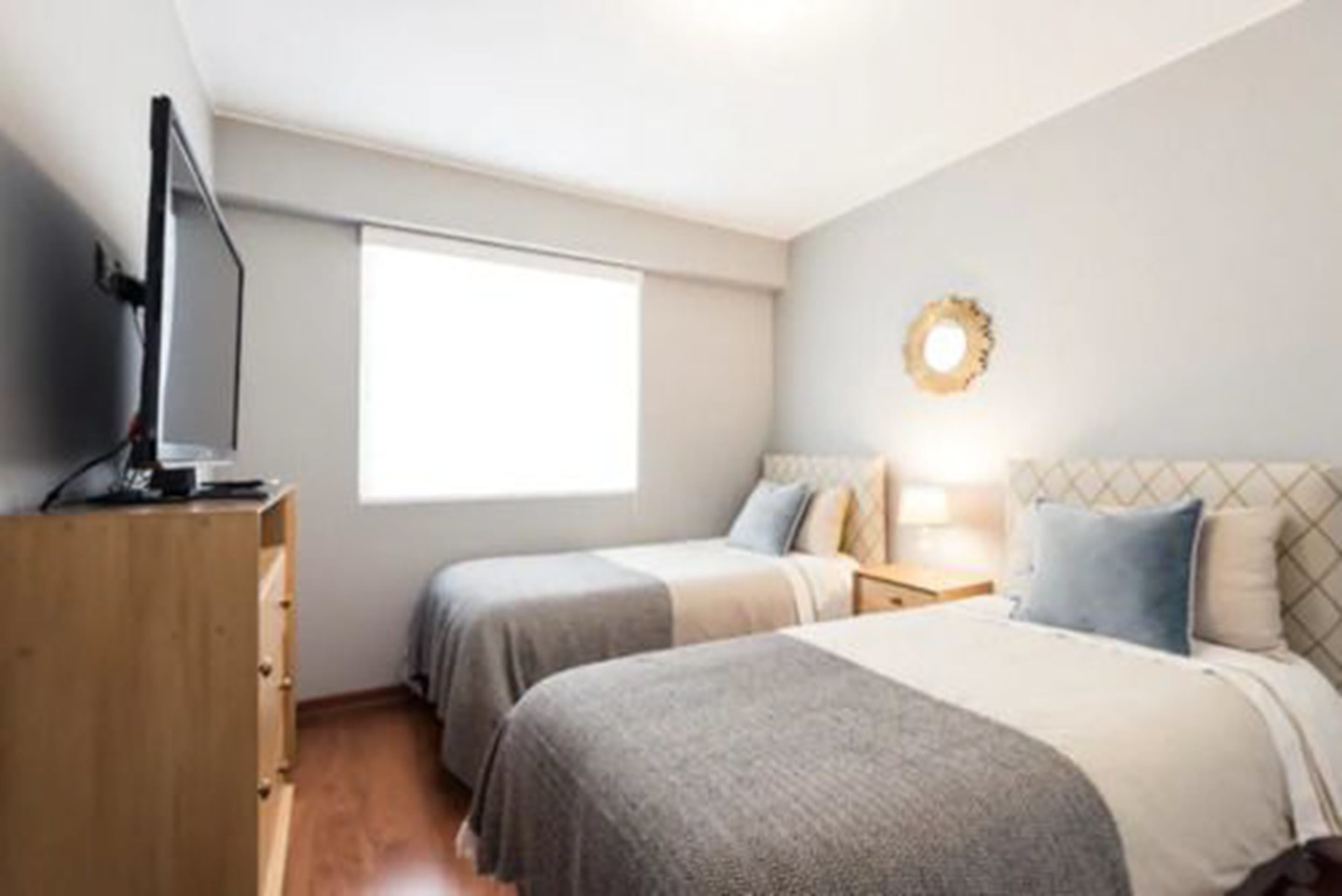 A bedroom with two beds, a wooden dresser, a television, and a window.