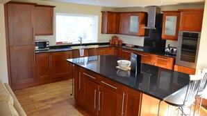 A modern kitchen with wooden cabinets, a black countertop, stainless steel appliances, and a large island. - The Coachhouse (Scarborough)