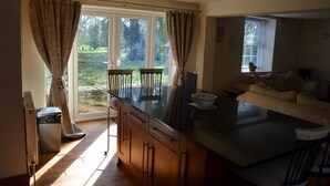 A modern kitchen with a large island, wooden cabinets, and a view of a garden through the sliding glass doors. - The Coachhouse (Scarborough)