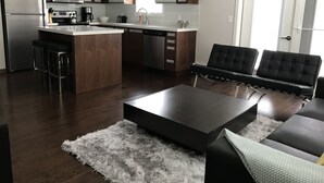 Eine moderne Küche mit einer zentralen Kochinsel, Barhocker, einem schwarzen Sofa und einem flauschigen Teppich.
