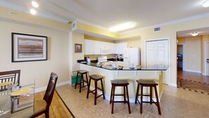 A modern kitchen with white cabinets, a central island with stools, and a dining area with a wooden table and chairs.