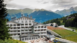 A multi-story hotel with balconies, a dining area, and a view of mountains. - Ecrin Blanc Resort Courchevel (Courchevel)