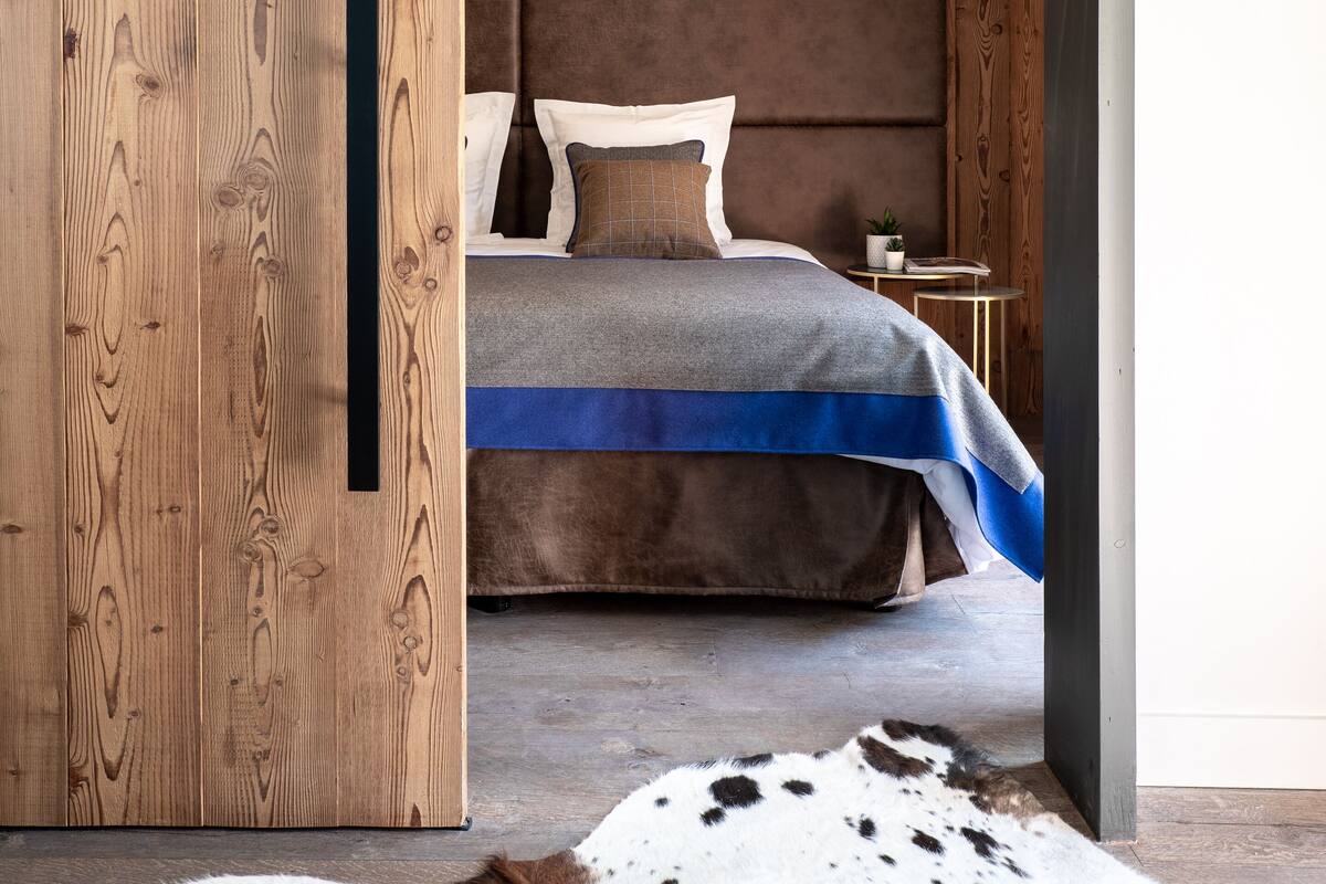 Una camera da letto con una parete in legno, un letto con copripiumino grigio e blu, un poggiatesta marrone e un piccolo comodino con una pianta.