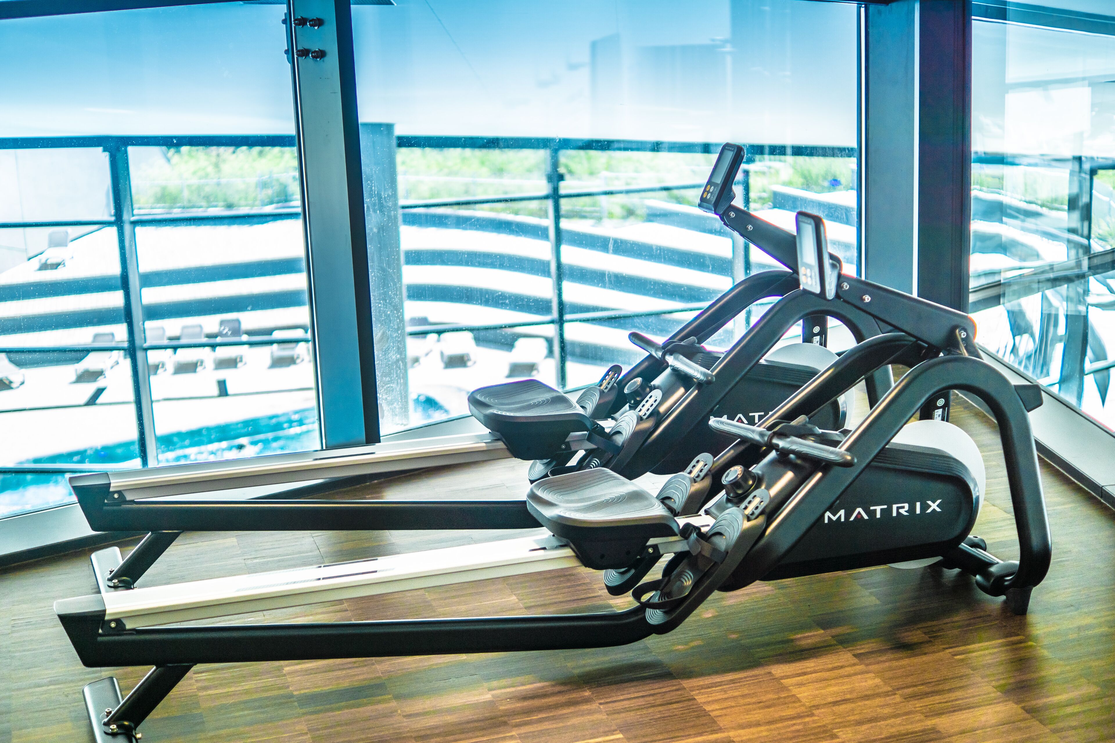 Una cinta de correr en un gimnasio con ventanas amplias y vista a un puente.