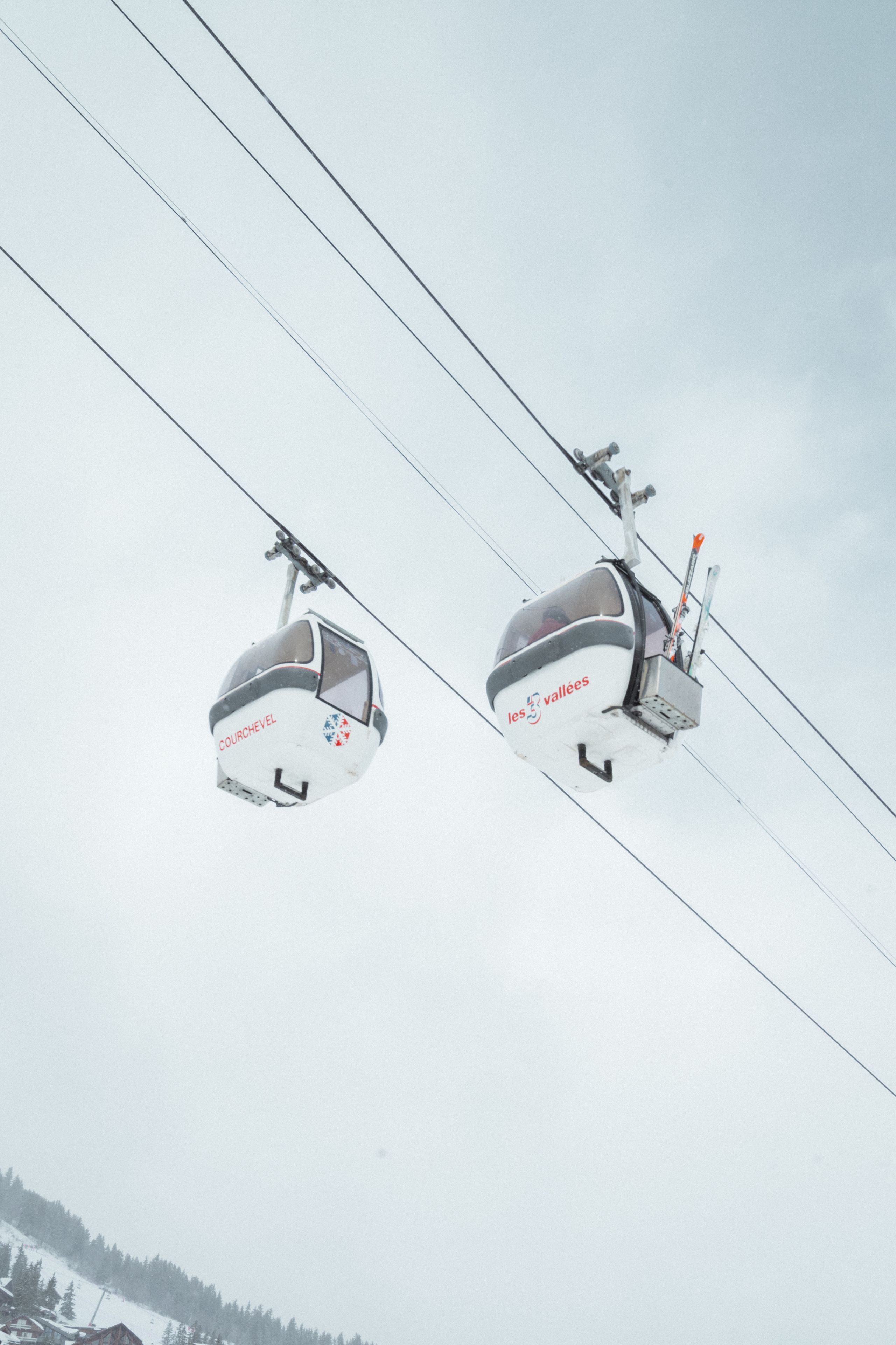 Due funivie con la scritta "les vallées" sospese da cavi sotto un cielo nuvoloso.
