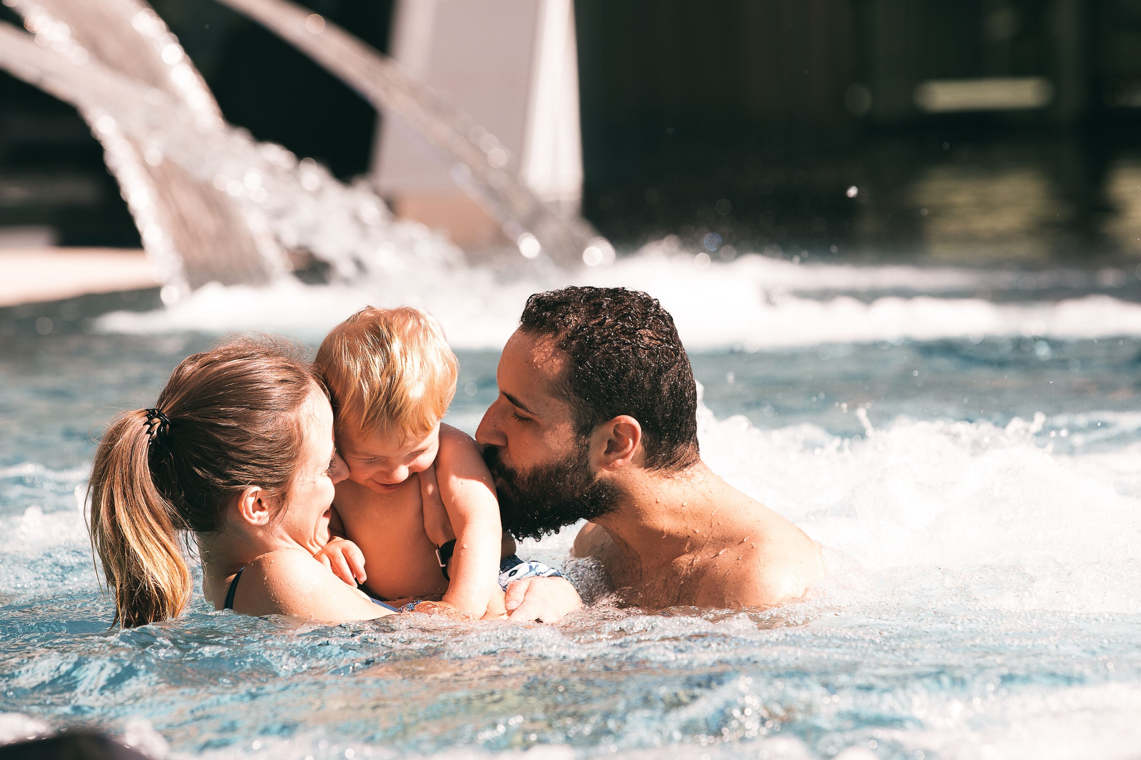 A family in a hot tub with water jets, surrounded by a pool area.