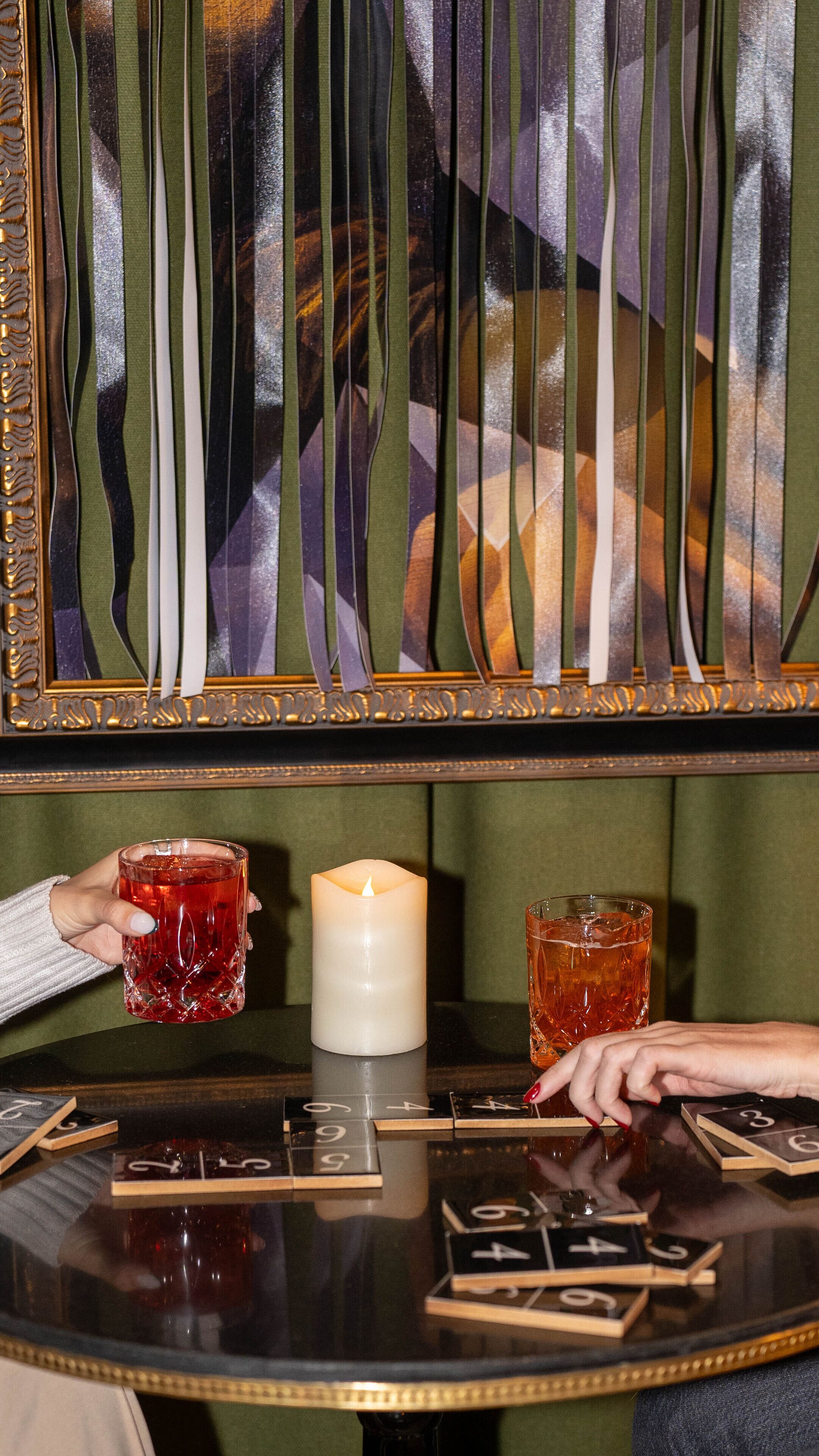 Une table avec une bougie, deux verres remplis d’une boisson rouge et un jeu de cartes.