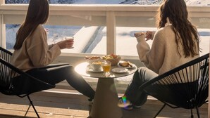 Two people sitting on a deck with a table in front of them, overlooking a snowy mountain landscape. - Ecrin Blanc Resort Courchevel (Courchevel)