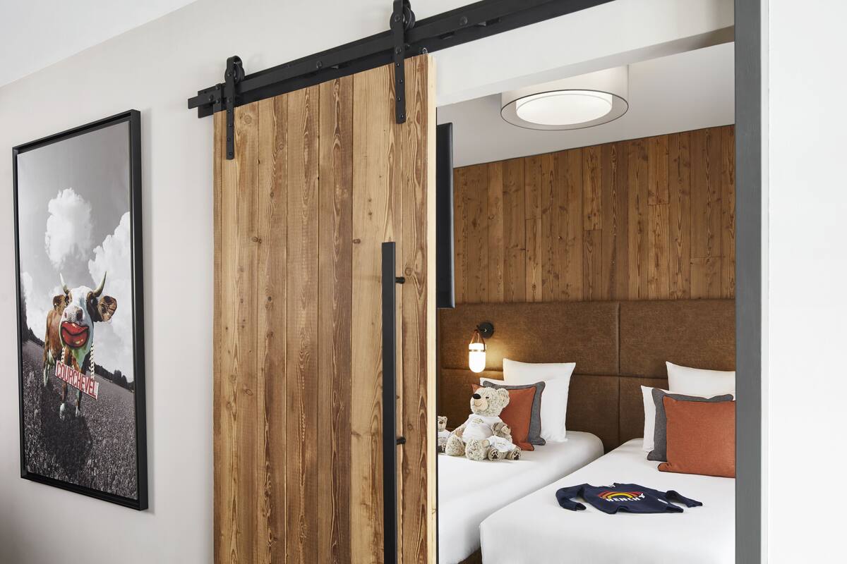 Camera d'albergo con una porta scorrevole in legno, un letto con biancheria bianca e un orsetto sul letto.