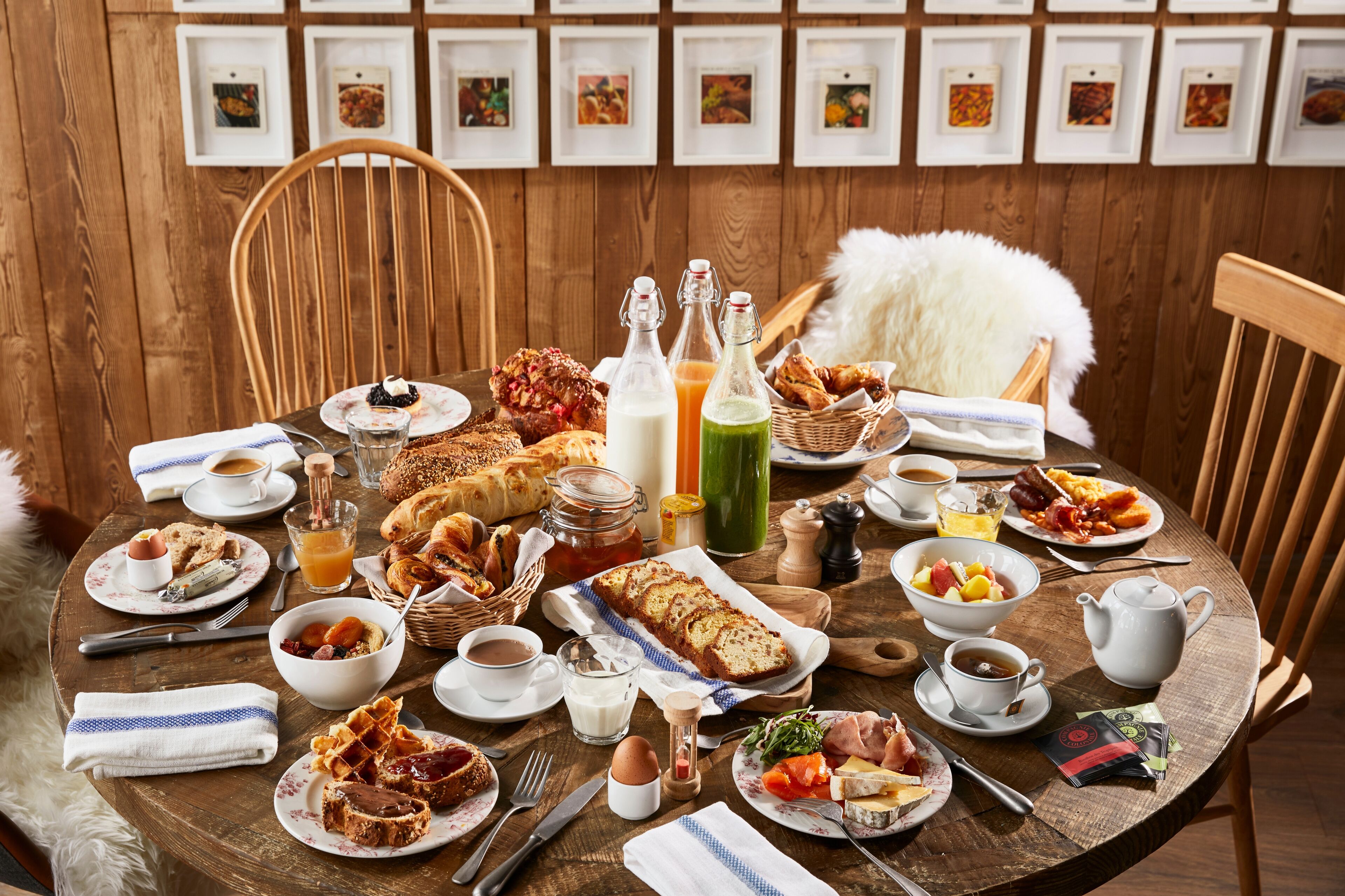 A wooden dining table with breakfast items, including bread, pastries, and beverages.