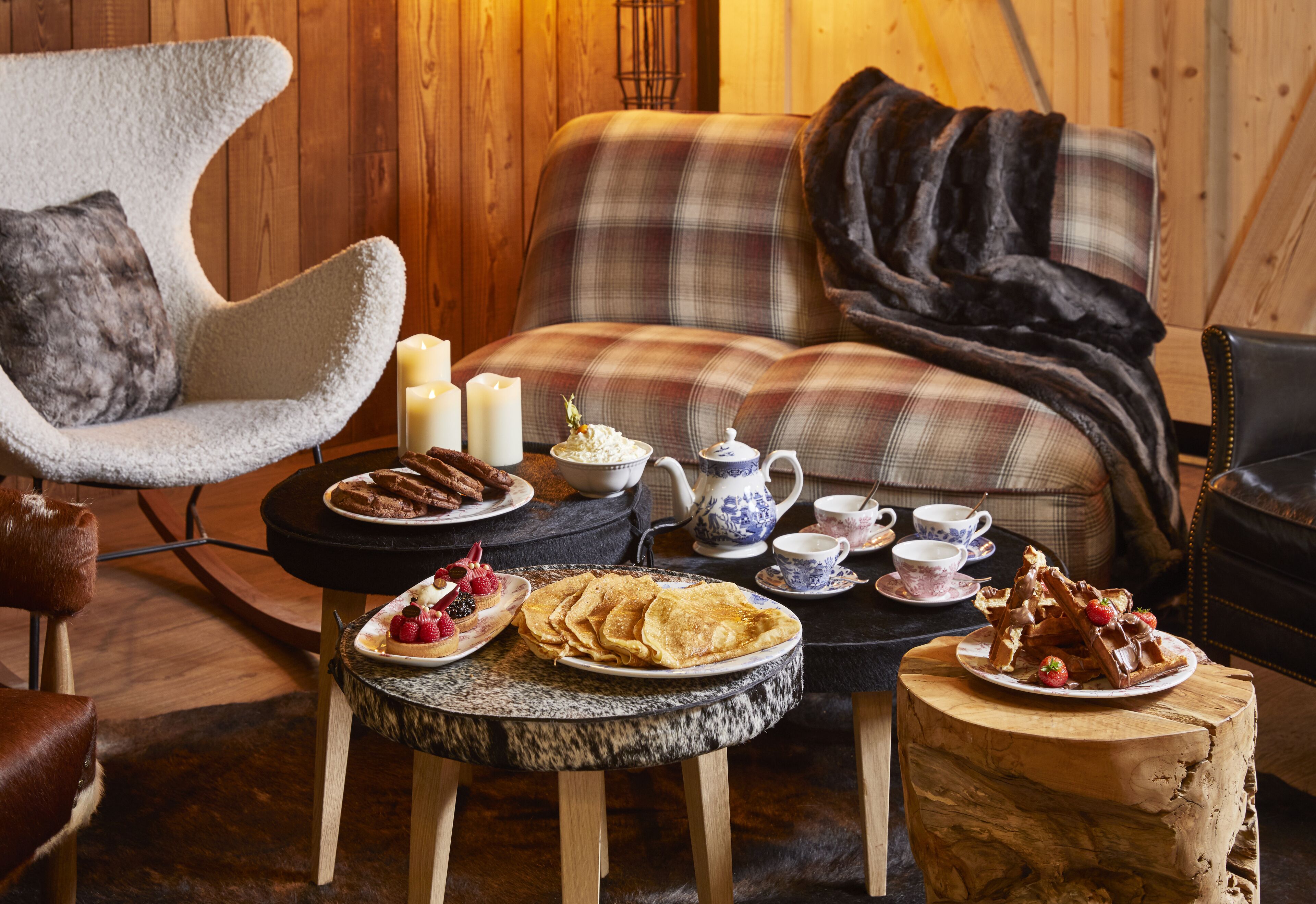 A cozy room with a plaid sofa, a fluffy armchair, and a wooden coffee table with breakfast items.