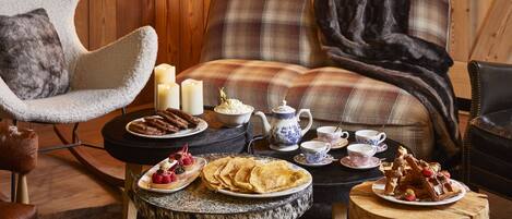 A cozy room with a plaid sofa, a fluffy armchair, and a wooden coffee table with breakfast items.