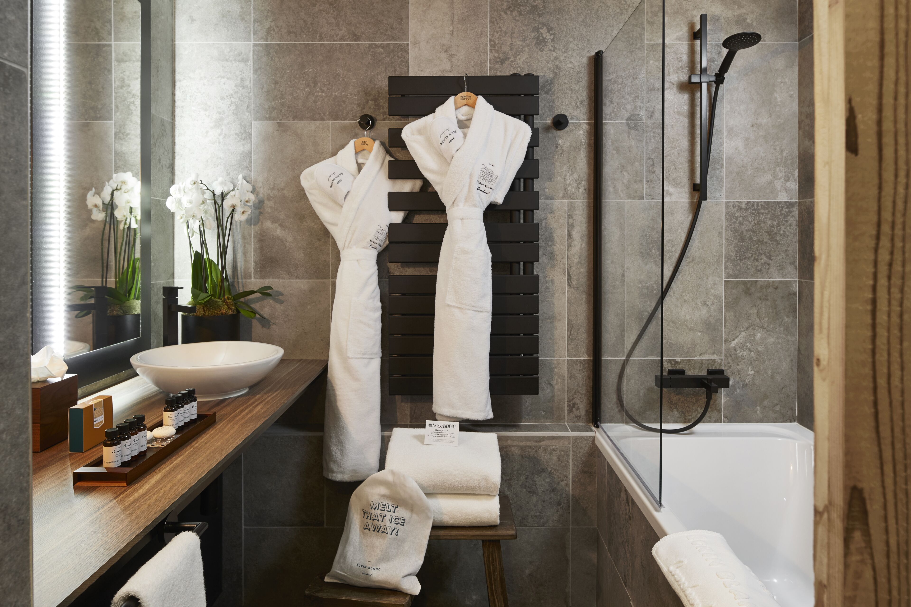 Un baño moderno con un lavabo grande, una bañera y dos albornoces blancos colgados en un perchero.