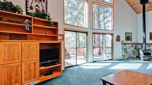 A spacious living room with a large TV, wooden shelves, and a stone fireplace. - Yosemite View (Yosemite National Park)