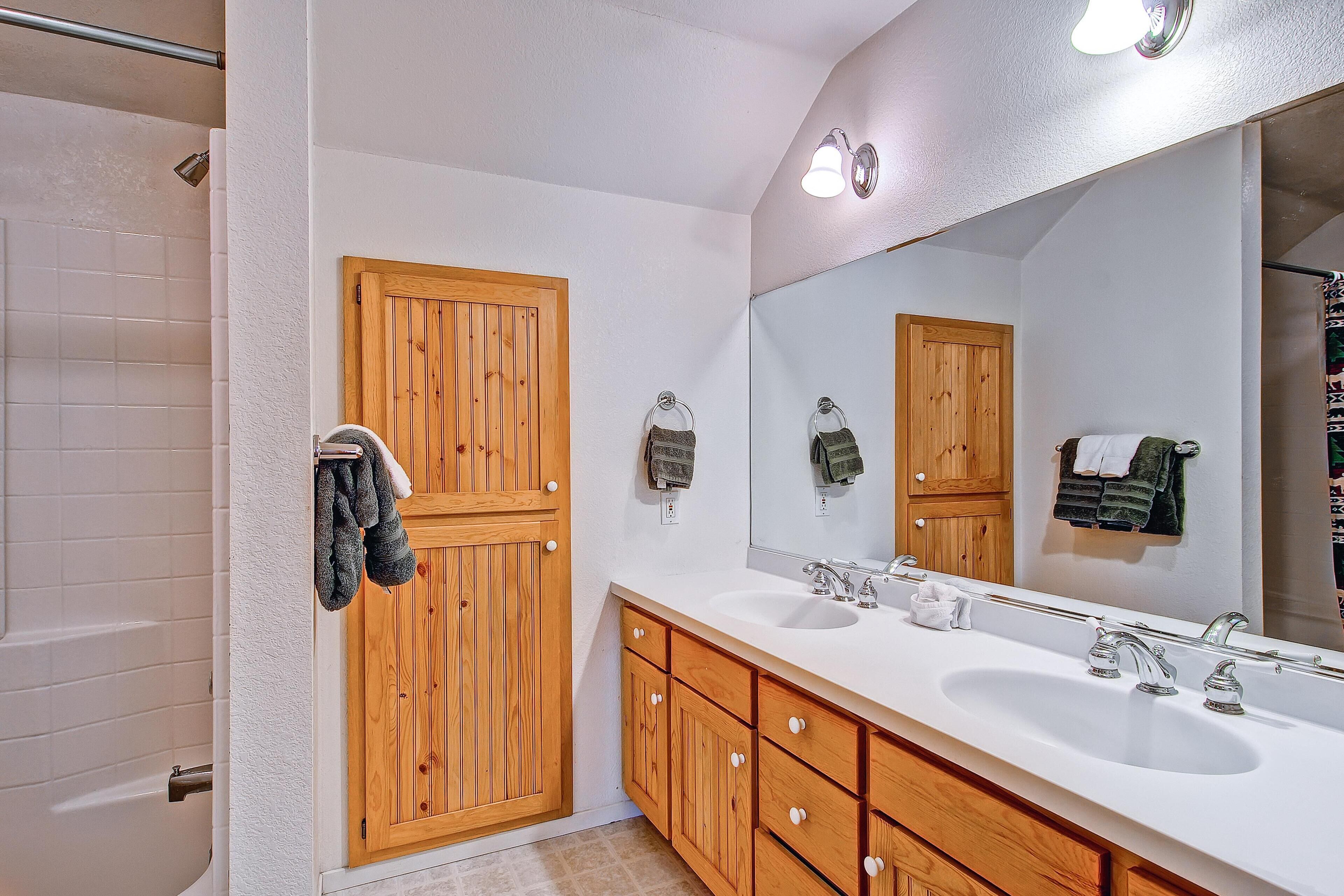 A bathroom with two sinks, wooden cabinets, a large mirror, and a shower area.