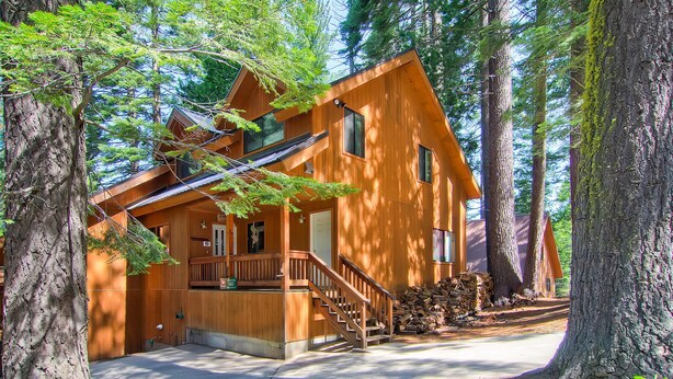 A wooden cabin with a staircase leading to a porch, surrounded by tall trees. - Yosemite View (Yosemite National Park)
