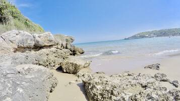 A rocky beach with clear blue water and a distant hill.