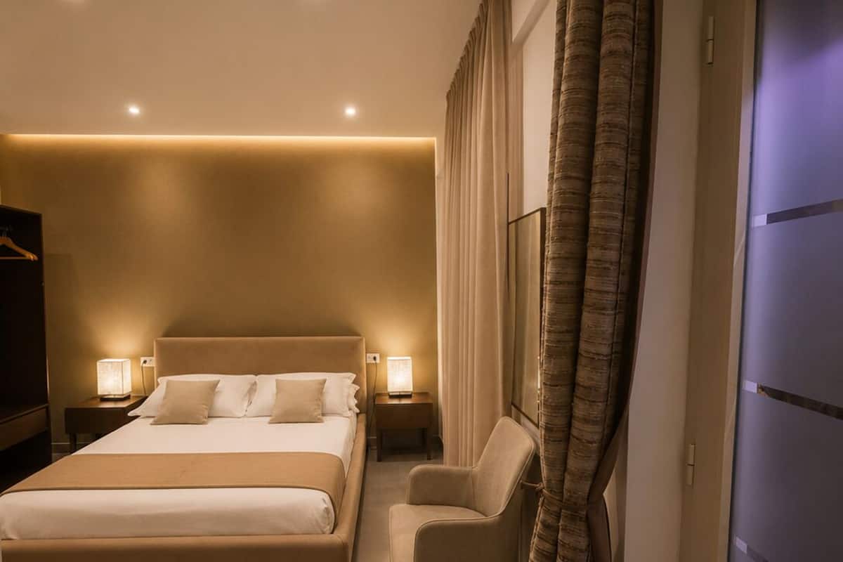 A hotel room with a large bed, bedside tables with lamps, a chair, a desk, and a wardrobe.