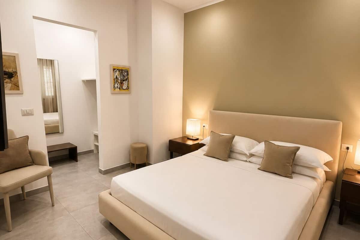 A modern bedroom with a large bed, bedside tables, a bench, and artwork on the walls.