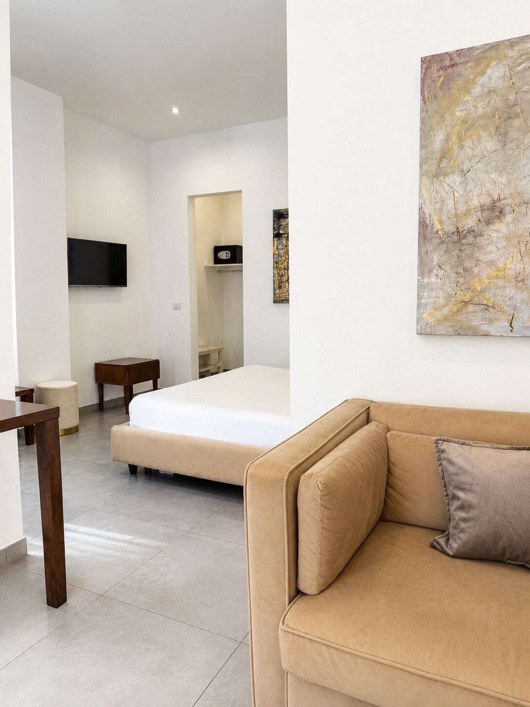 A modern hotel room with a bed, a sofa, a TV, and a painting on the wall.