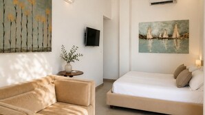 A modern hotel room with a sofa, a bed, a painting of sailboats, and a TV. - Petra Maris B&B (Peschici)