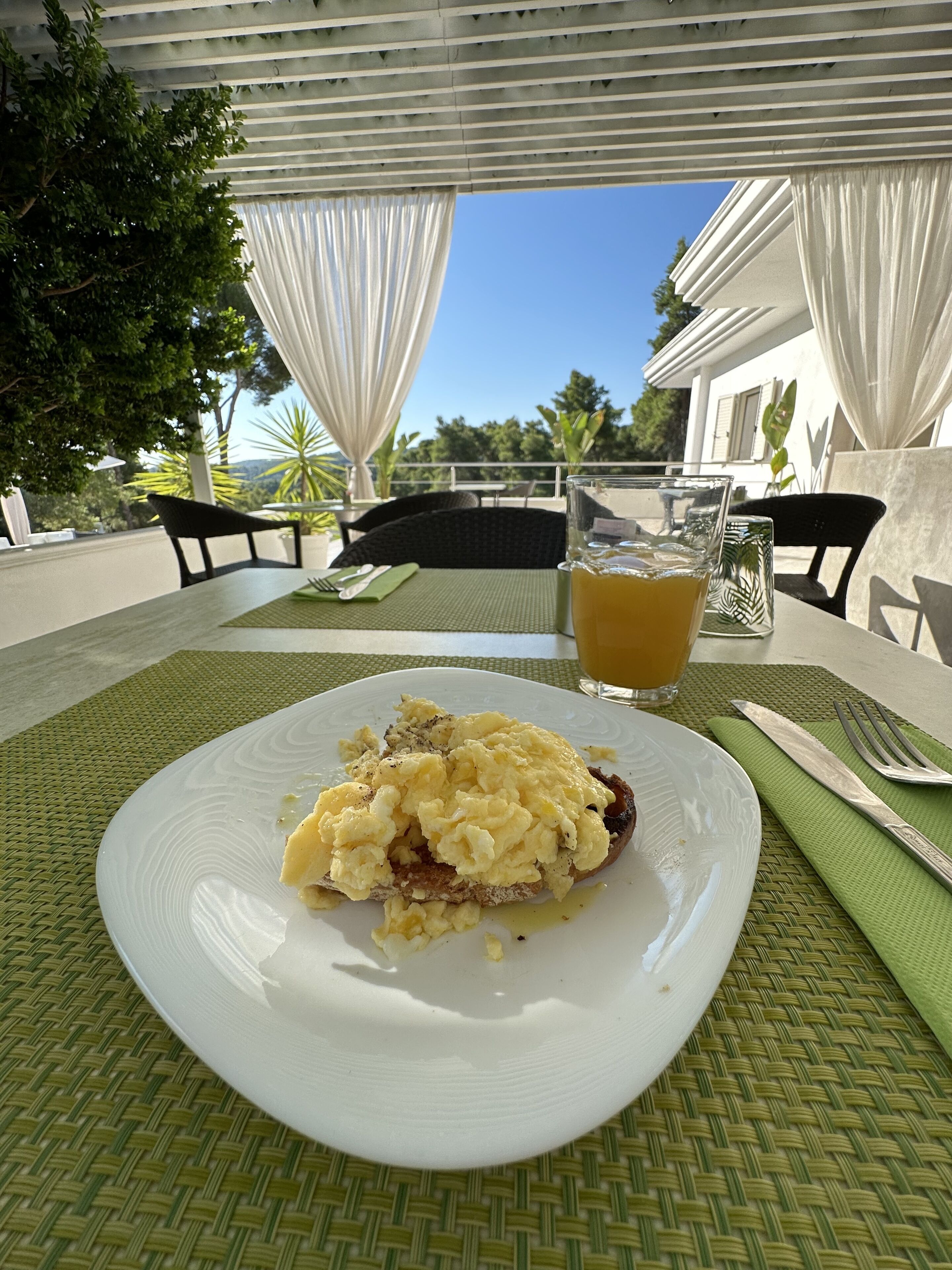 Una mesa con un plato de huevos revueltos y tostadas, un vaso de jugo de naranja y un mantel individual verde.