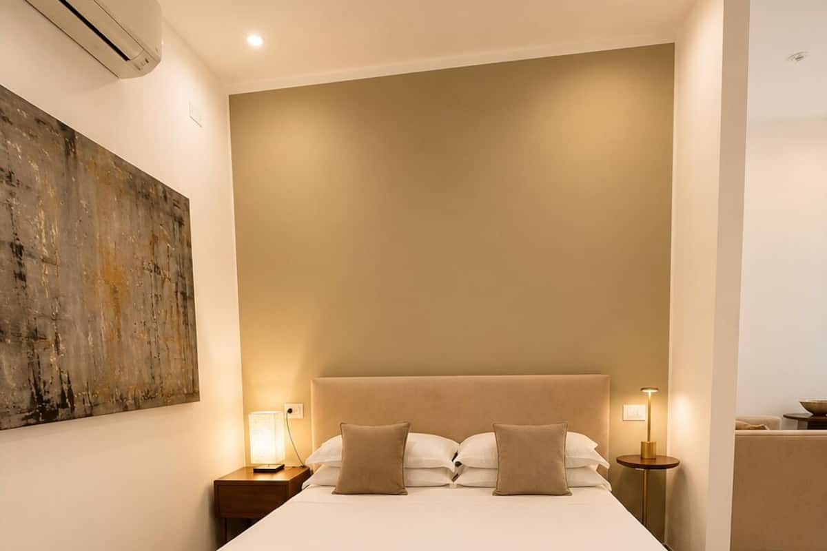 A modern bedroom with a large bed, bedside lamps, and a wall-mounted air conditioner.