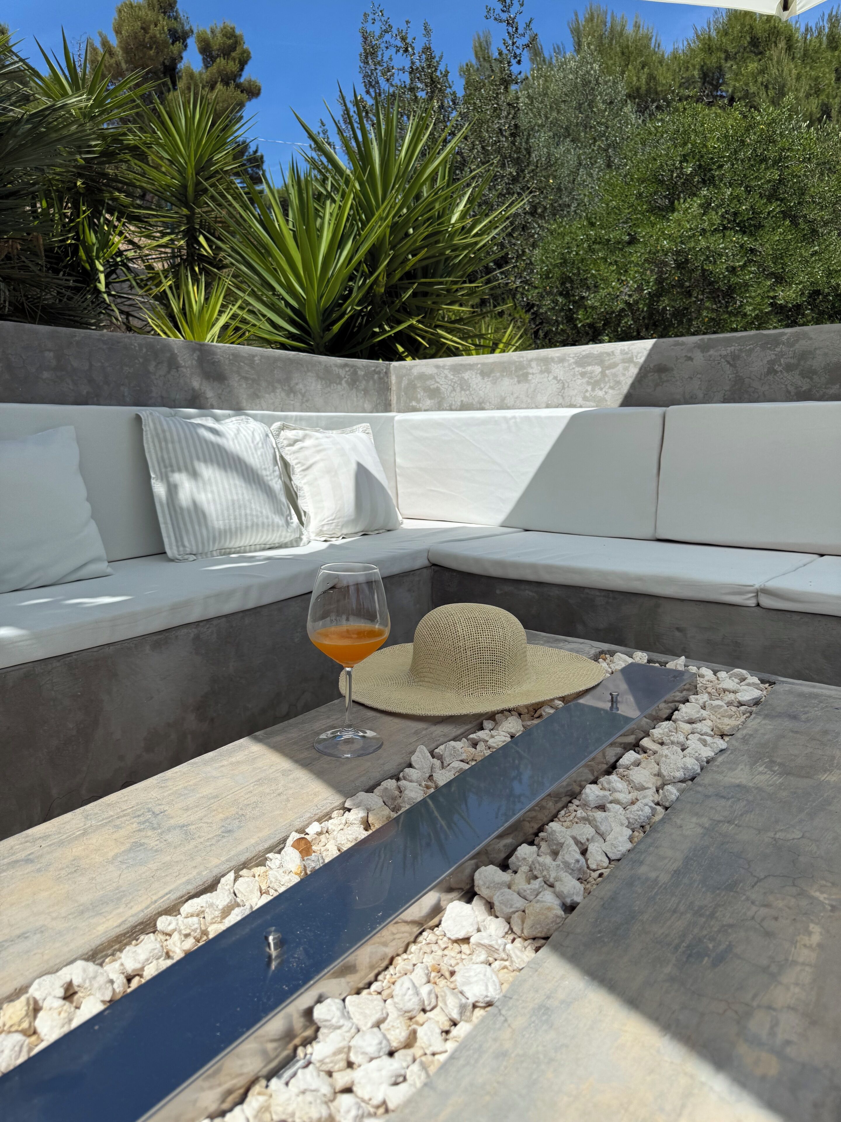 A modern outdoor seating area with a stone table, cushions, and a glass of drink.