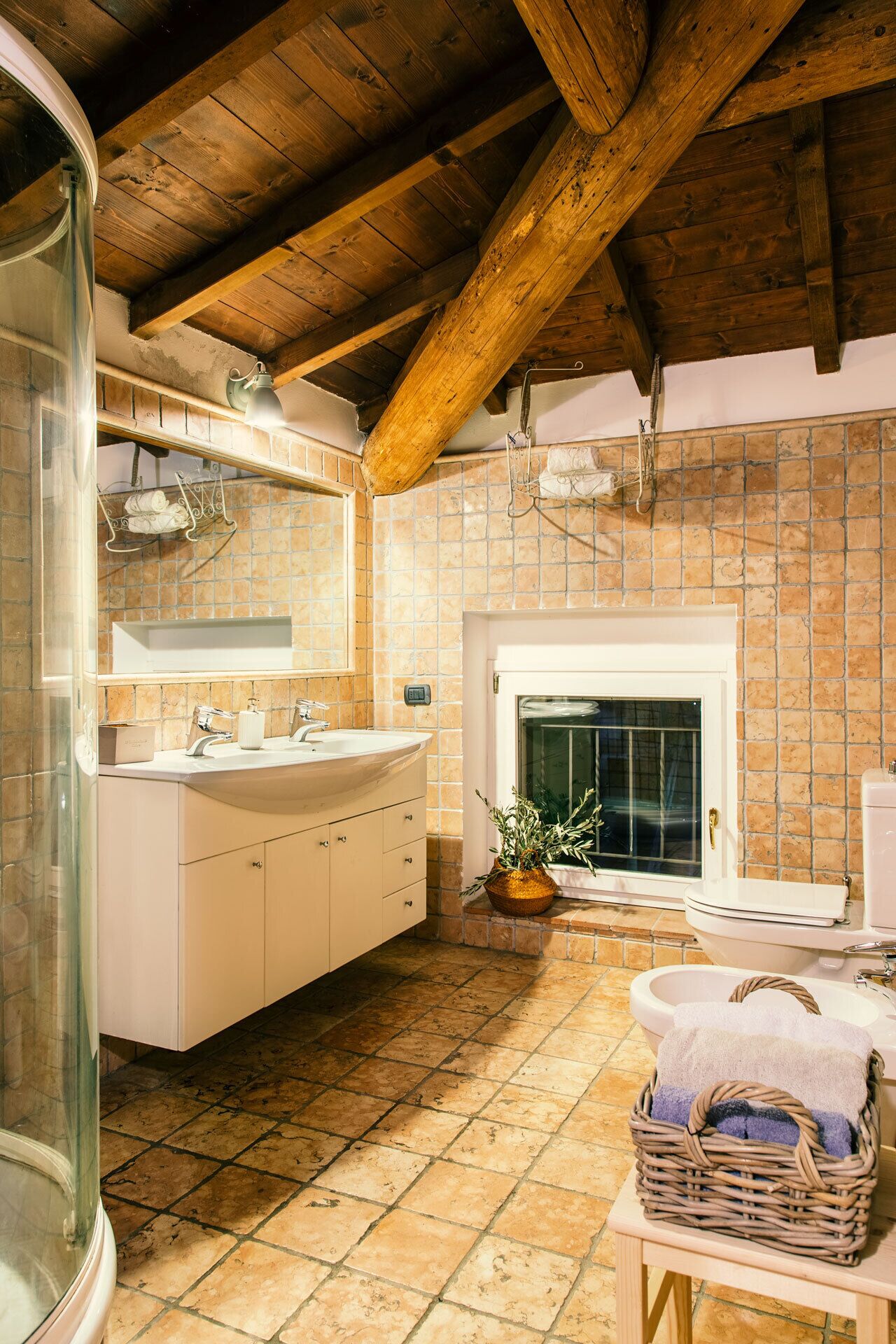 A bathroom with a double sink, a mirror, a white bathtub, a tiled floor, and a wooden ceiling.