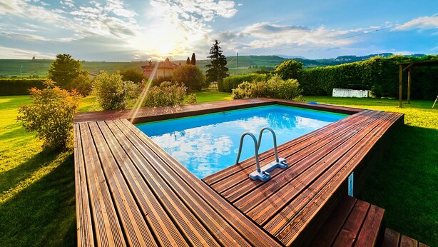 A wooden deck with a swimming pool, surrounded by well-maintained lawns and hedges, under a clear sky. - Relais Valpolicella B&B (Marano di Valpolicella)