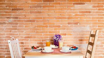 Ein Holztisch mit Frühstücksgebäck, einer Blumenvase und einer Backsteinwand im Hintergrund.