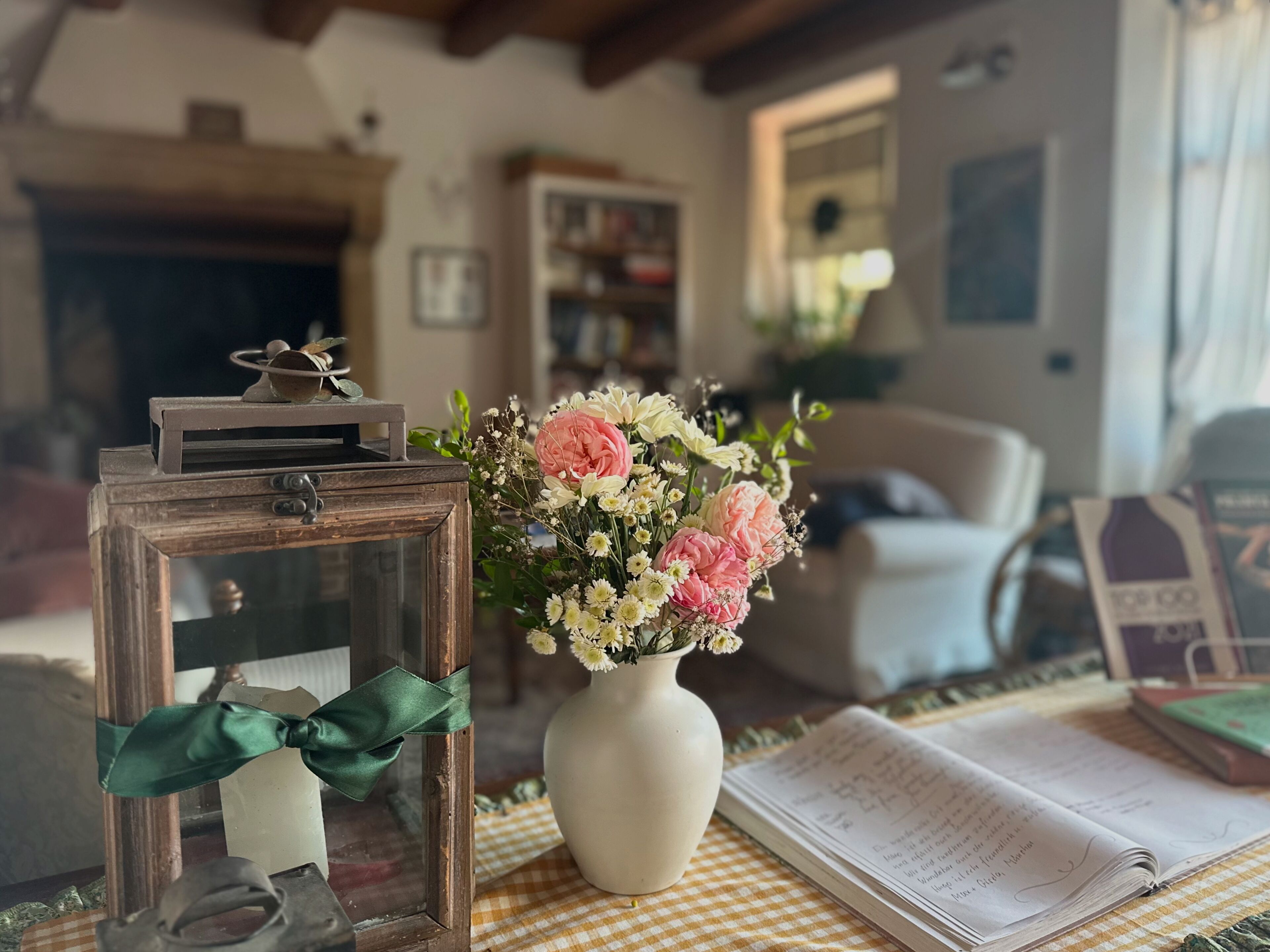 Un saló d'estar acollidor amb una taula de fusta, un vas de flors blanc, un llibre i una fotografia emmarcada.