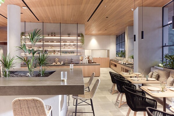 A modern kitchen with wooden cabinets, a central island, and a dining area with black chairs and a light-colored table.