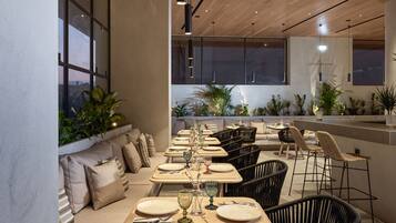 Un interno ristorante moderno con lunghe tavole, sedie nere e una zona bar.