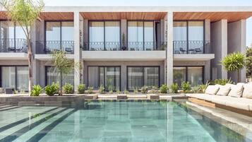 A modern building with a swimming pool, balconies with outdoor furniture, and a well-maintained garden.