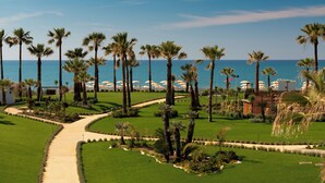 A well-maintained garden with palm trees, a pathway, and beach umbrellas. - Mangia's Himera Resort (Campofelice di Roccella)