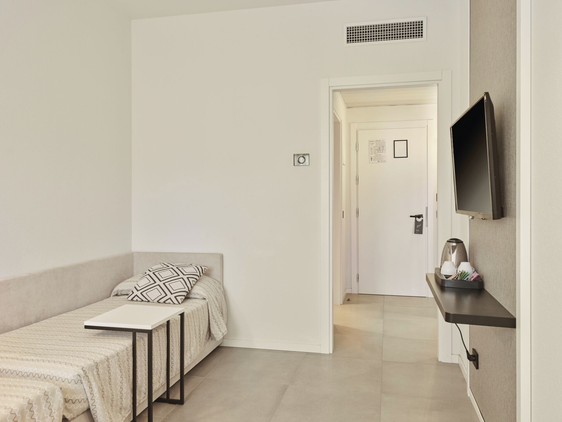 Una habitación minimalista con una cama, un televisor en la pared y una mesita.