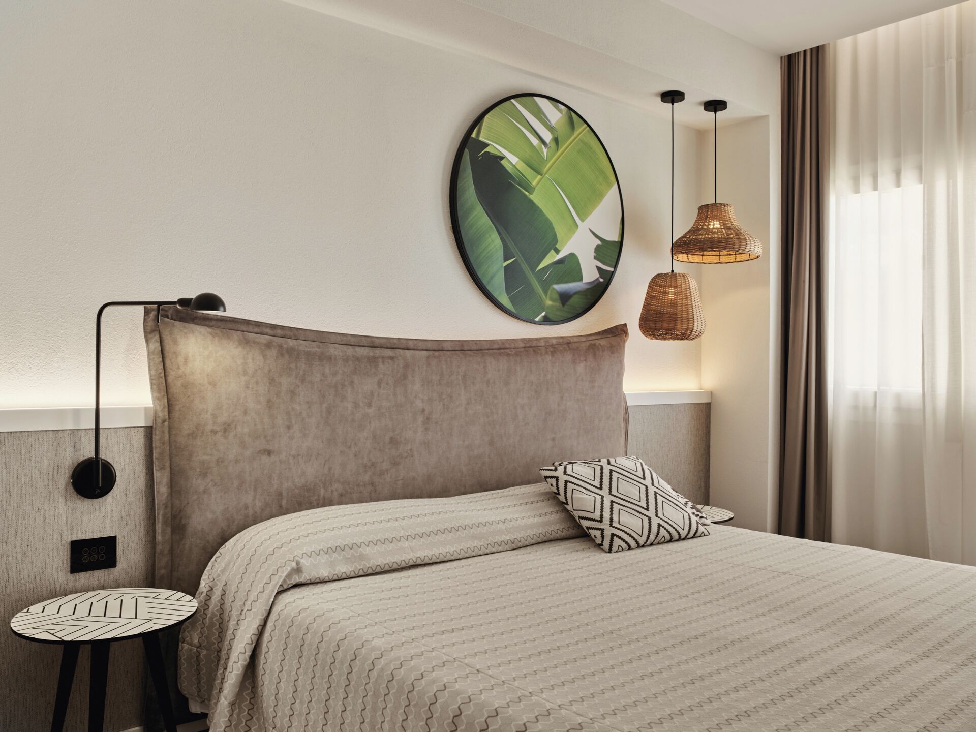 Une chambre d’hôtel bien rangée, avec un lit, une œuvre d’art ronde accrochée au mur, une lampe suspendue et une petite table.