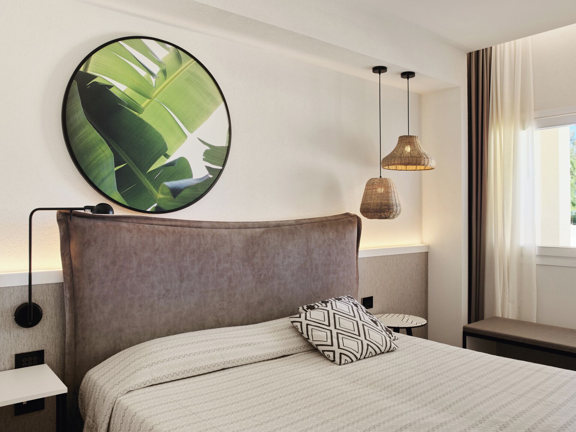 A neatly arranged hotel room with a large bed, a round wall art piece, a small table, and two pendant lights.
