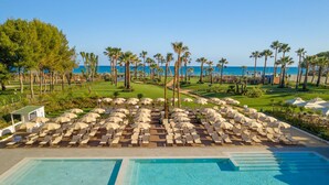 A poolside area with lounge chairs and umbrellas, a clear view of the sea, and a well-maintained lawn with palm trees. - Mangia's Himera Resort (Campofelice di Roccella)