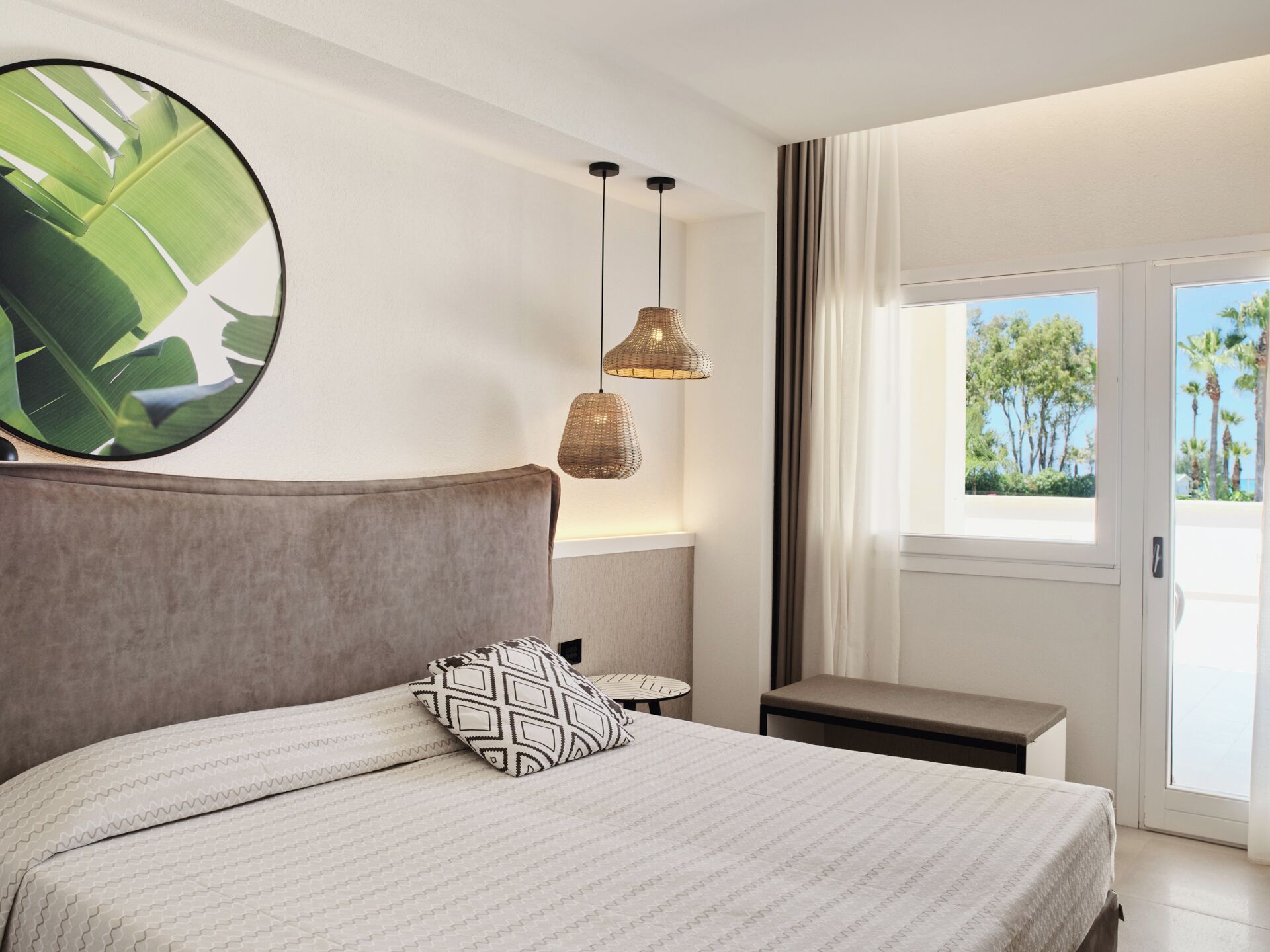 Un dormitorio con cama, un espejo grande en la pared, una lámpara colgante y vistas a palmeras a través de una ventana.