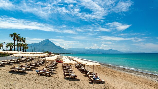 A beach with rows of sun loungers and umbrellas, a mountain in the background, and a clear blue sky. - Mangia's Himera Resort (Campofelice di Roccella)