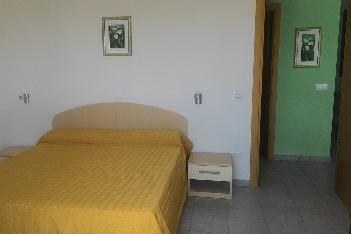 A bedroom with a bed, nightstands, and a door leading to another room.