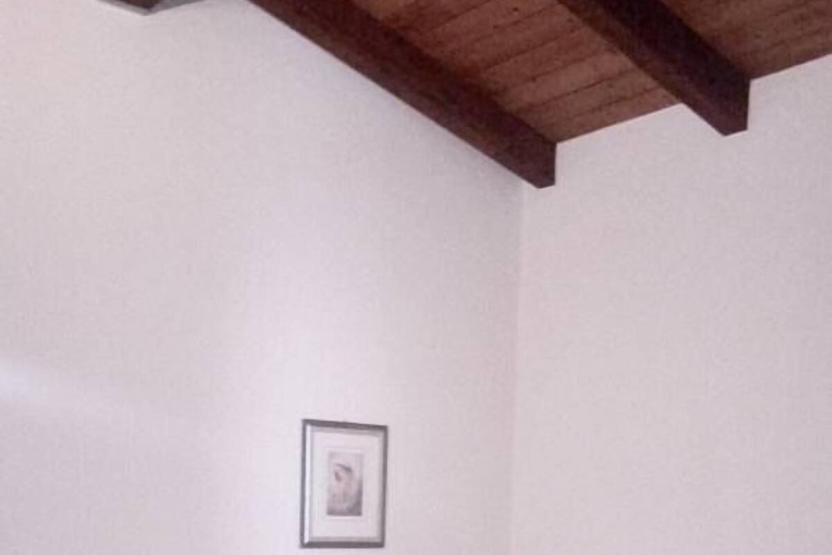 A single bed with a beige bedspread and white linens, a framed picture on the wall, and a wooden ceiling.