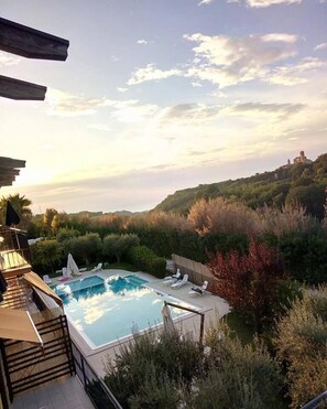 Ein privater Pool mit Liegestühlen, umgeben von üppiger Vegetation und einer Hügelkette mit einer schlösserähnlichen Struktur im Hintergrund.