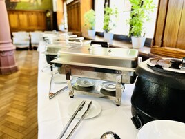 Disposición de un bufé con múltiples estaciones de servicio, incluyendo una olla negra grande y una bandeja de acero inoxidable.