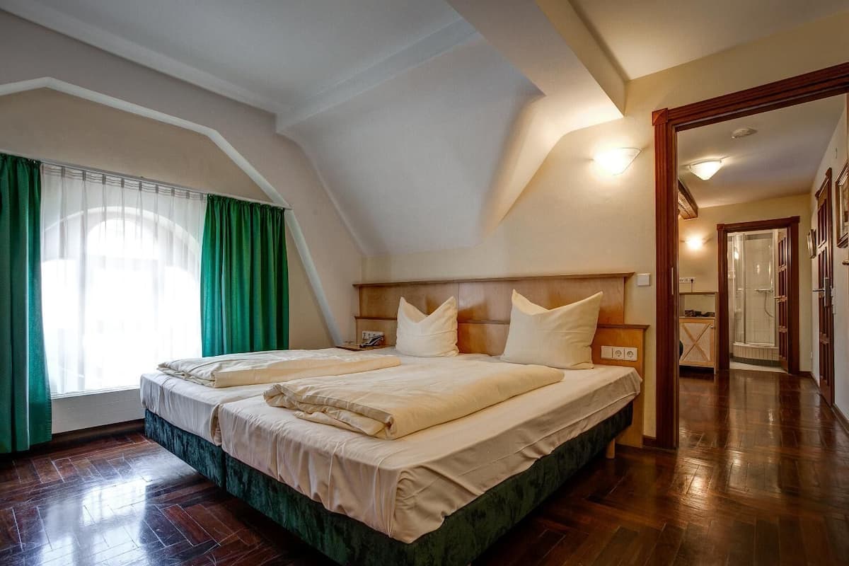 Ein Schlafzimmer mit einem großen Bett, einem Holzkopfteil, einem Nachttisch und einem Fenster mit grünen Vorhängen.