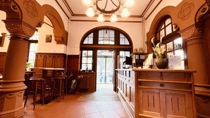 A spacious lobby with high ceilings, a chandelier, and a large arched doorway leading outside. - Hotel Hoepfner Burghof (Karlsruhe)
