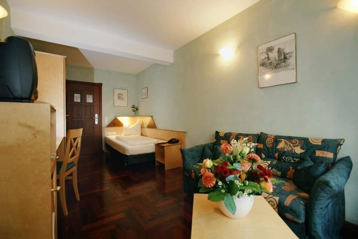 Ein Zimmer mit einem Bett, einem Sofa, einem Tisch mit Blumenvase, einem Stuhl und einer Tür.
